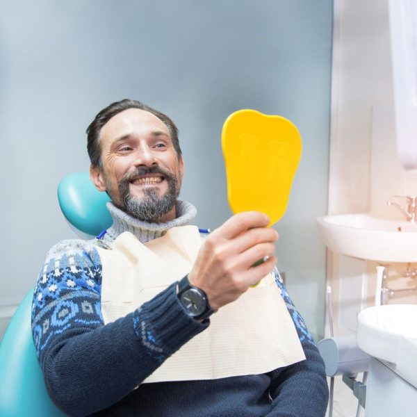 Man smiling in dental chair, mirror